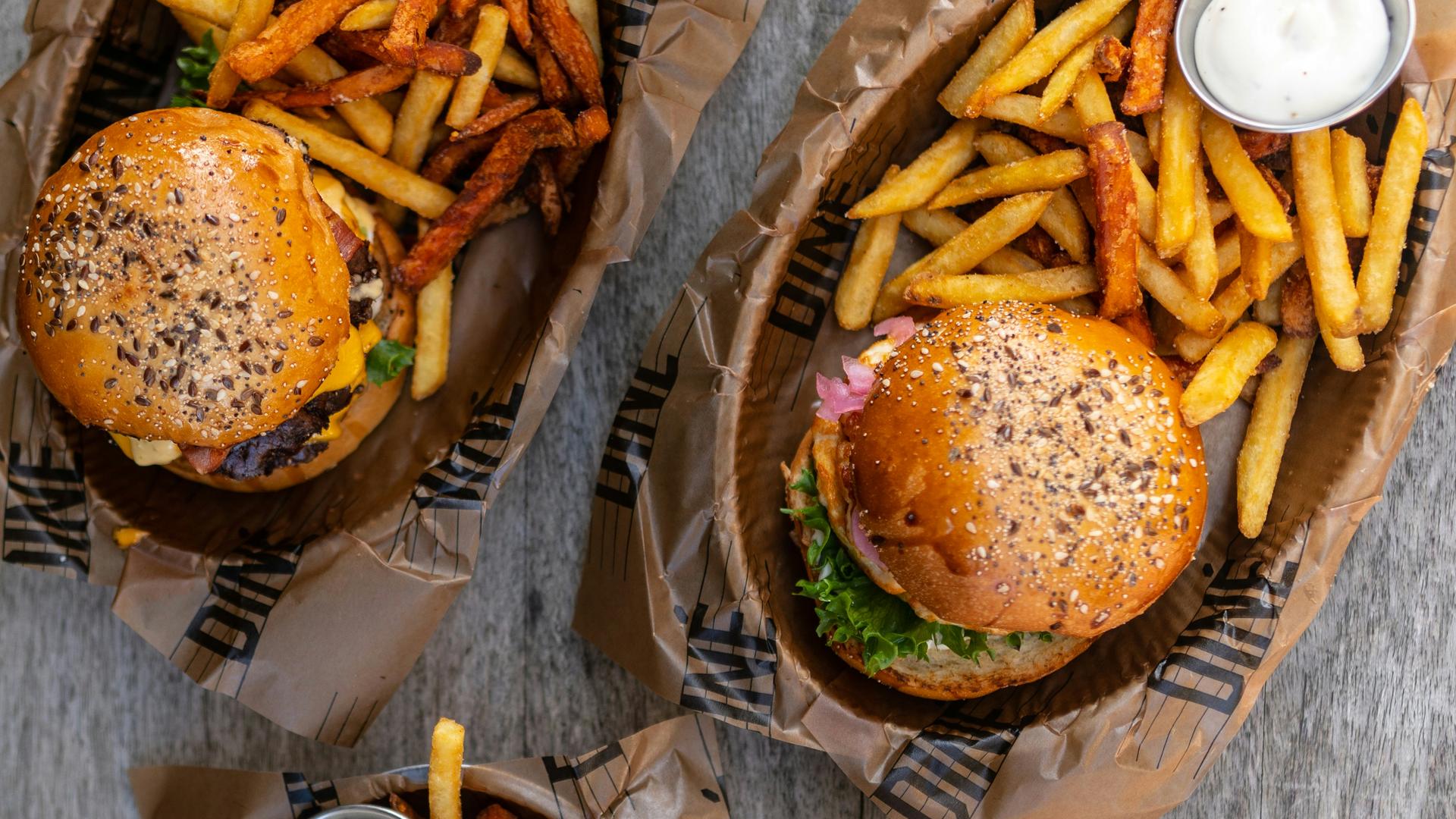 Overhead shot of three burgers with fries in paper trays and milkshakes on a grey table