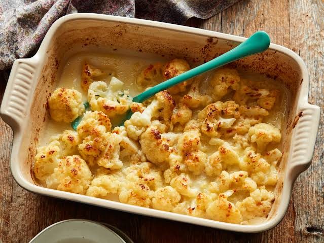 Baked cauliflower in a cheese sauce in a cream ceramic dish with a green spoon