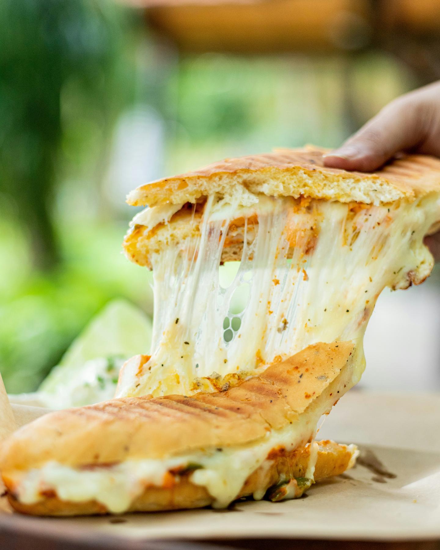 A hand lifting half of a grilled cheese sandwich, the melted cheese stretching between the halves