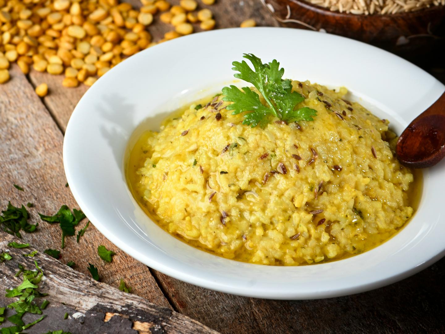 A bowl of yellow khichdi topped with coriander, with raw lentils and rice in the background