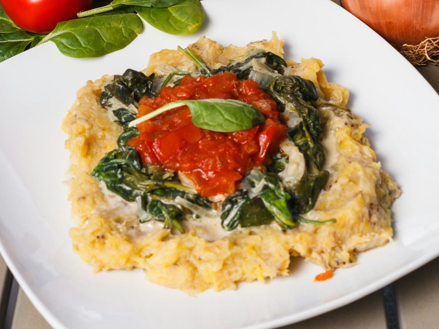 Creamy polenta on a white plate topped with wilted spinach and tomato sauce